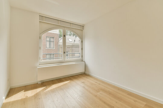 Bright empty room with large arched window and wooden floor