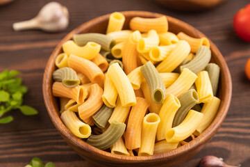 Rigatoni colored raw pasta with tomato, eggs, spices, herbs on brown wooden. Side view, selective focus