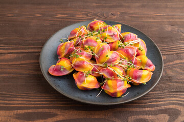 Rainbow colored dumplings with microgreen on brown wooden. Side view, close up