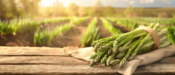 Fototapeten Fresh Asparagus on Farm Wooden Table, Freshly harvested green asparagus arranged on a rustic wooden table, with a softly blurred farm landscape in the background. © petrrgoskov