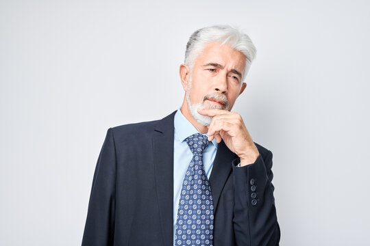 Thoughtful senior businessman hand on chin, contemplating isolated on a light background.