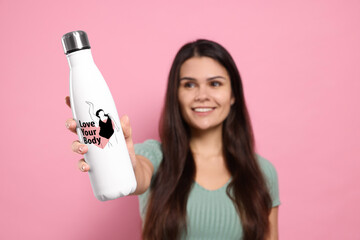 Smiling woman holding thermo bottle with drawn figure of plus-size model, heart and phrase Love...