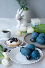 Easter holiday table setting and decoration, blue dyed eggs, flowers and rabbit figurine on table
