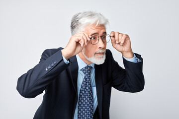 Confident senior businessman adjusting glasses, isolated on grey background.