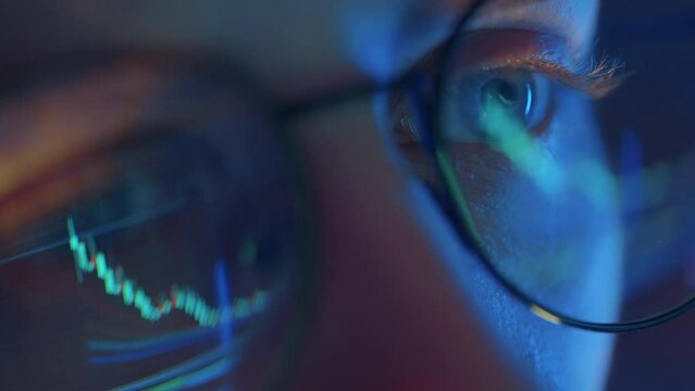 Trader wearing glasses is working on laptop computer. Screen with stock market charts and Bitcoin BTC or Ethereum ETH data analysis reflection. Broker trading online. Altcoins crypto currency trading