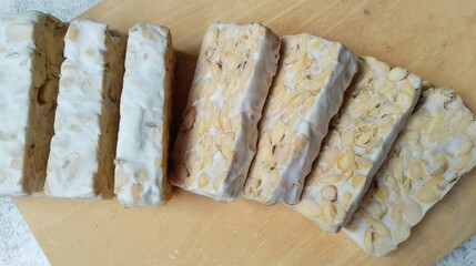Raw tempe in slices on wooden chopping board. Raw Tempeh, traditional food from Indonesia. Tempe or tempeh is soybeans fermentation in cake form.