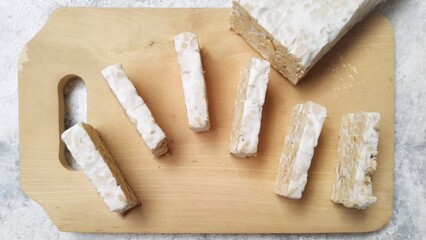 Raw tempe in slices on wooden chopping board. Raw Tempeh, traditional food from Indonesia. Tempe or tempeh is soybeans fermentation in cake form.