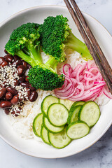Vegan poke. Bowl with rice, broccoli, cucumber, beans and pickled red onion, white background.