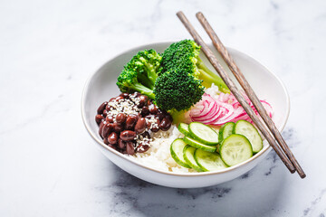 Vegan poke bowl with rice, broccoli, cucumber, beans and pickled red onion, white background.