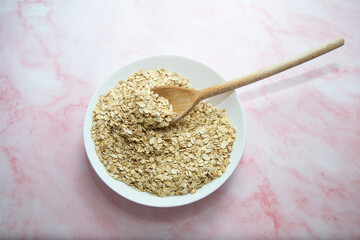 bowl and spoon of oatmeal on pink marble background, top view