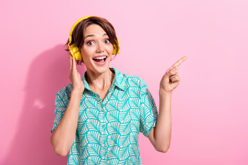 Photo of cheerful impressed person hand touch headphones direct finger empty space isolated on pink...