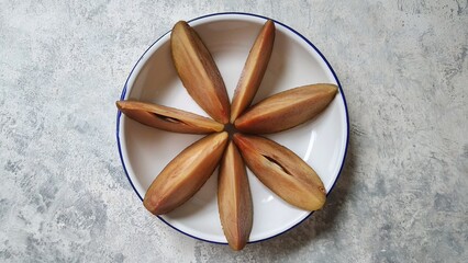 Sapodilla (Manilkara zapota) cut in slices against rustic white background.