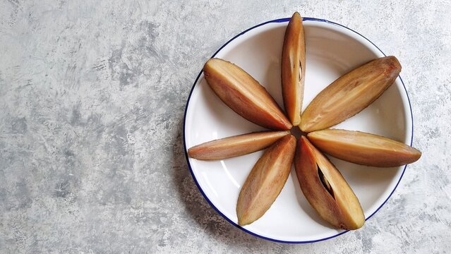 Sapodilla (Manilkara zapota) cut in slices against rustic white background