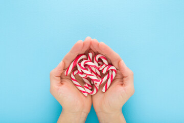 Red white candy canes in young adult woman opened palms on light blue table background. Pastel...