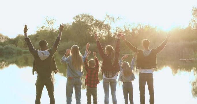 Volunteer environmental activists people team of adults and children which standing on the lake's bank with raised hands and feeling good
