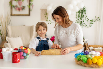 Little blond toddler child with mother, preparing dough for easter brioche buns, sweet easter bread with nuts and dry fruits