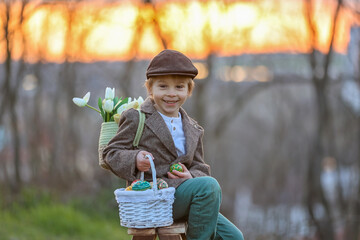 Beautiful stylish toddler child, boy, playing with Easter decoration in the park, springtime