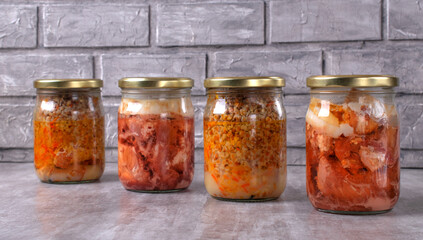 Different canned stewed meat in glass jars on the table against the gray background. Canned pork and buckwheat, ready-made meal