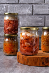 Different canned stewed meat in glass jars on the table against the gray background. Canned pork and buckwheat, ready-made meal