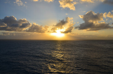Golden sunset at sea, reflections on water surface, cloudy sky with sunset light sunrays