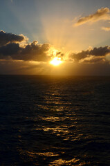 Golden sunset at sea, reflections on water surface, cloudy sky with sunset light sunrays