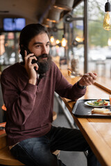 Hipster man having lunch at a fast food restaurant talking on the phone with a customer during his lunch