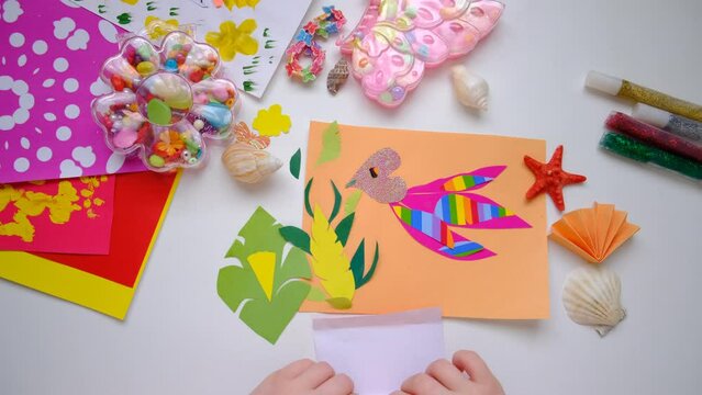 Child making homemade greeting card, applique with bird,  hummingbird or colibri and flowers from pieces of paper, tropical garden. Gift for Mothers day, Birthday, Easter, holidays. 