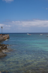 Seascape. Dock of the village of Arrieta with group of boats anchored near the dock in the background. Turquoise Atlantic Ocean. Big white clouds. Village of Arrieta. Lanzarote, Canary Islands, Spain