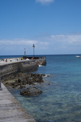 Seascape. Dock of the village of Arrieta with group of boats anchored near the dock in the background. Turquoise Atlantic Ocean. Big white clouds. Village of Arrieta. Lanzarote, Canary Islands, Spain