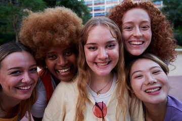 Happy portrait of five multiethnic female friends looking at camera cheerfully. Diverse group of women with heads together smiling united for equality and women's right.