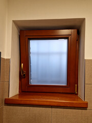 the toilet window is used to ventilate the smell. wooden brown frame and a sticker on the glass with a blur effect.