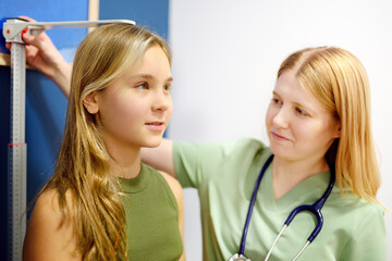 Female doctor measuring of teenage girl height. Schoolgirl patient is at pediatrician appointment. Healthcare for kids.