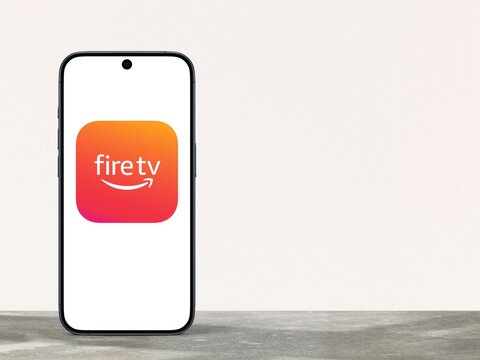 Fire TV App Logo is displayed on a modern smartphone, remote control for a line of digital media players and microconsoles developed by Amazon