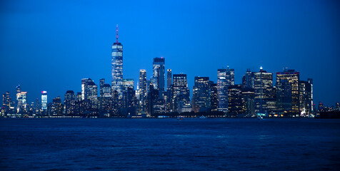The Manhattan skyline under a twilight blue sky, city lights beginning to twinkle.