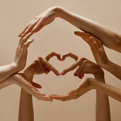 Photo of human hands making circle symbol and shape of heart of unity, support and love against sandy color studio background. Concept of human touch, beauty and care, spa procedures.
