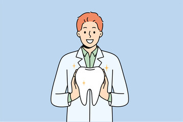 Man orthodontist from dental clinic holds model of healthy tooth, offering you procedure to get rid of caries. Guy orthodontist in white coat smiles, recommending becoming client of new dental center