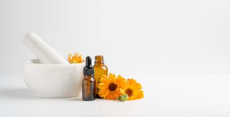 Calendula flowers in mortar and amber glass dropping bottles with essential oil. 