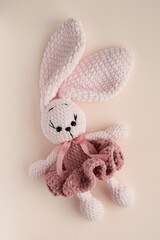 Pale pink bunny in a fluffy dress, crocheted on a light background. Handmade children's toy. Happy childhood concept. Top view, close-up