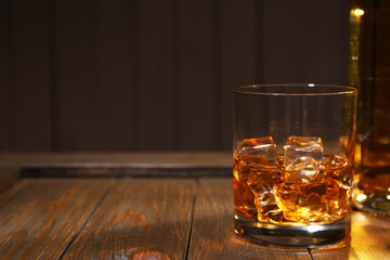 Whiskey with ice cubes in glass on wooden crate against black background, closeup. Space for text
