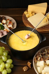 Fondue pot with melted cheese, forks and different products on wooden table