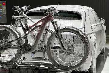 Electric vehicle and bicycles at self-service car wash during nighttime, covered in foam,...
