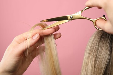 Hairdresser cutting client's hair with scissors on pink background, closeup