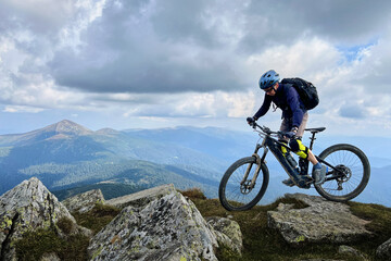 Cyclist man riding electric mountain bike outdoors. Male tourist biking along grassy trail in the...