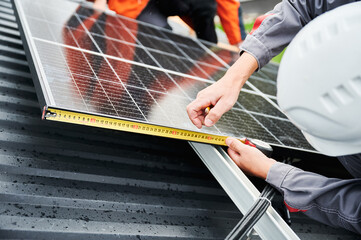 Man measuring photovoltaic solar panels with tape measure. Close up view of worker taking measurements before mounting solar modules on roof for generating electricity through photovoltaic effect. - obrazy, fototapety, plakaty