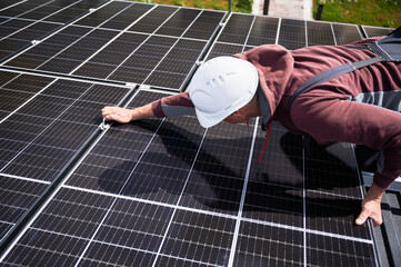 Man builder mounting photovoltaic solar panels on roof of house. Engineer in helmet installing...