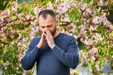 Man allergic suffering from seasonal allergy at spring in blossoming garden at springtime. Bearded...