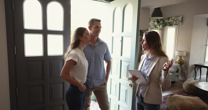 Female real estate agent consulting young married couple, standing at new modern house hallway tells about terms, facilities, buying or renting, negotiate about prices, rental rates and contract terms