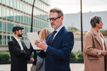 One mature business man using a digital tablet to work outside. Isolated mid adult executive employee browsing on internet with a touchpad at workplace. Successful male sending a email with a pad