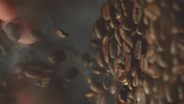 Super slow motion shot of falling roasted coffee beans from hand with smoke in macro. Vertical close up video