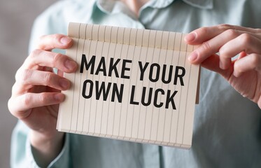 Hands holding a torn paper with MAKE YOUR OWN LUCK text on a green background